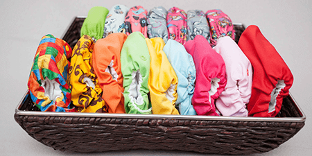 Colorful collection of reusable cloth diapers displayed in a basket, featuring various vibrant patterns and colors.
