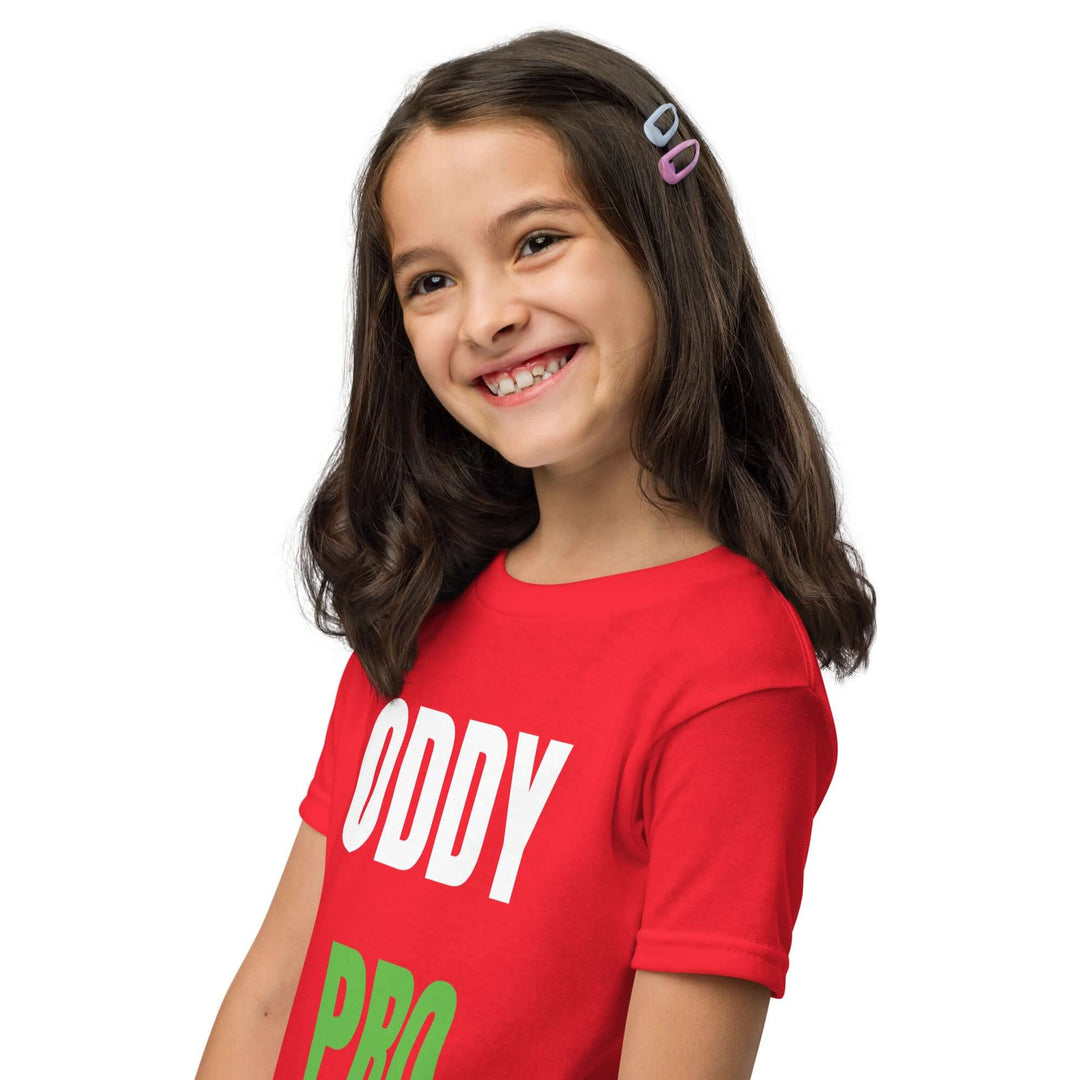 Girl wearing Oddy Pro Youth t-shirt in red, smiling with hair clips, showcasing modern fit and comfort.